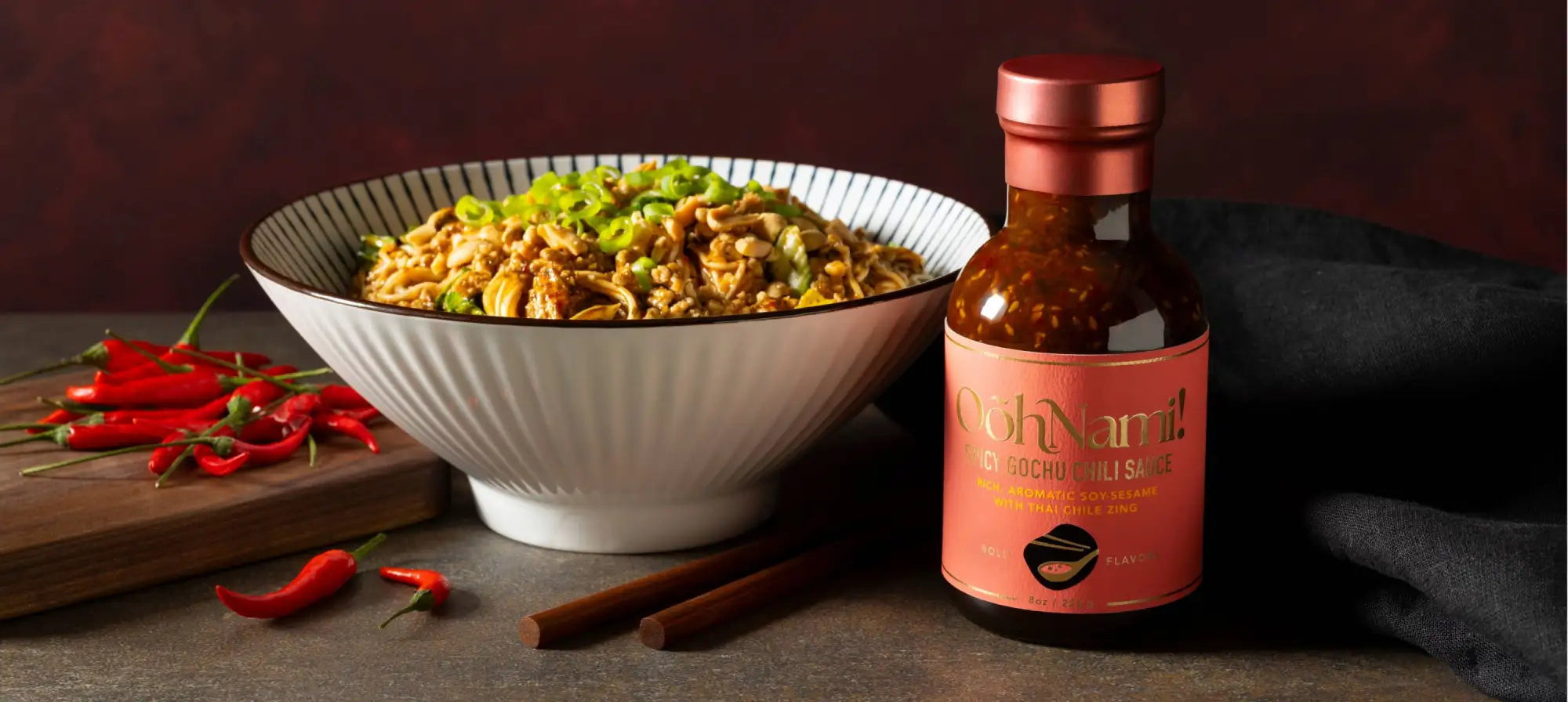 A bottle of c’oh nami! Go gochujang chili sauce with a pink label and metallic rose-gold cap, containing a vibrant red sauce in a clear glass container.