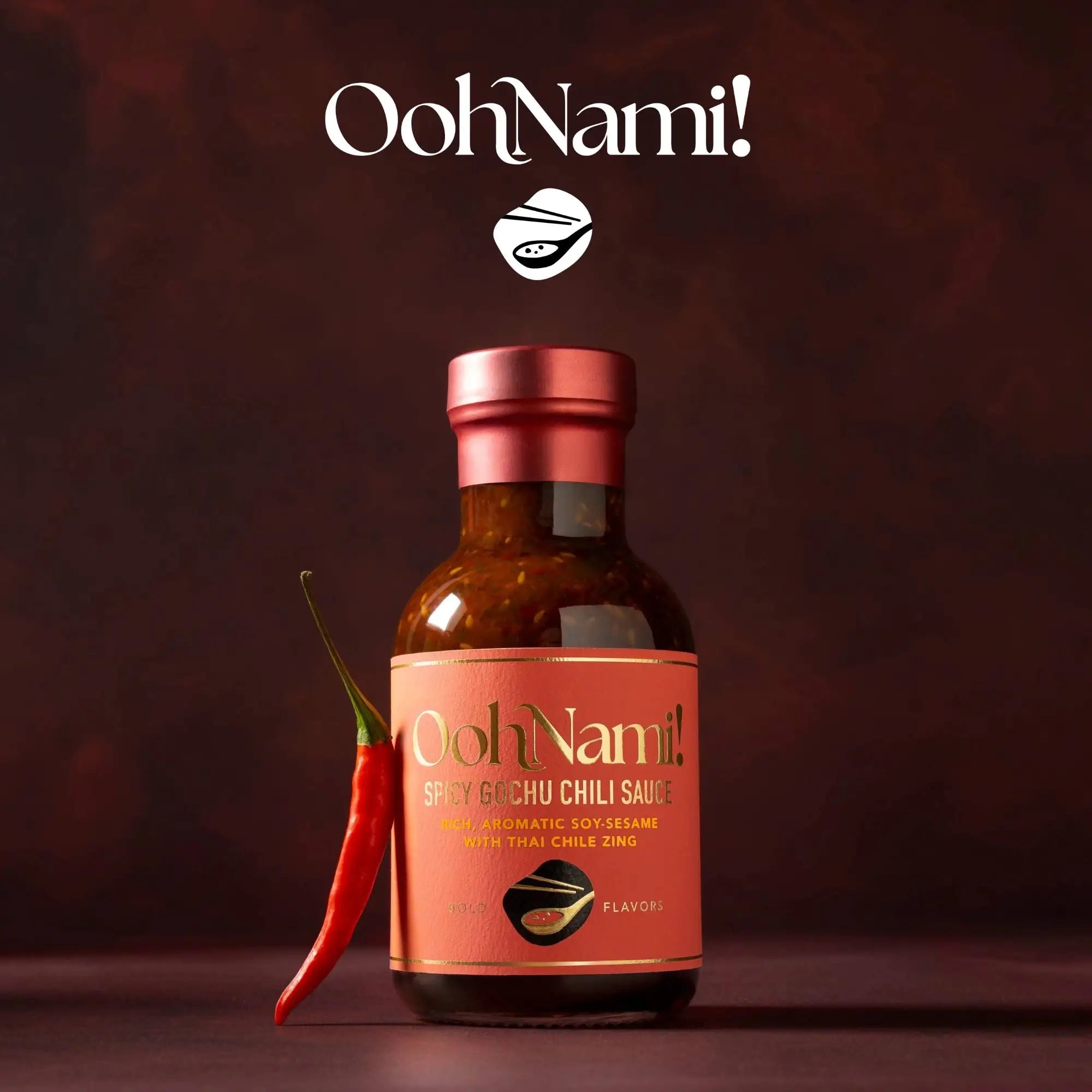 A bottle of oohnami! Spicy gochu chili sauce with a red metallic cap and an orange label featuring gold lettering, containing a rich amber sauce.