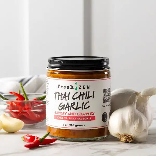 A glass jar of fresh zen thai chili garlic sauce with a black lid and white label, containing an orange-red condiment.