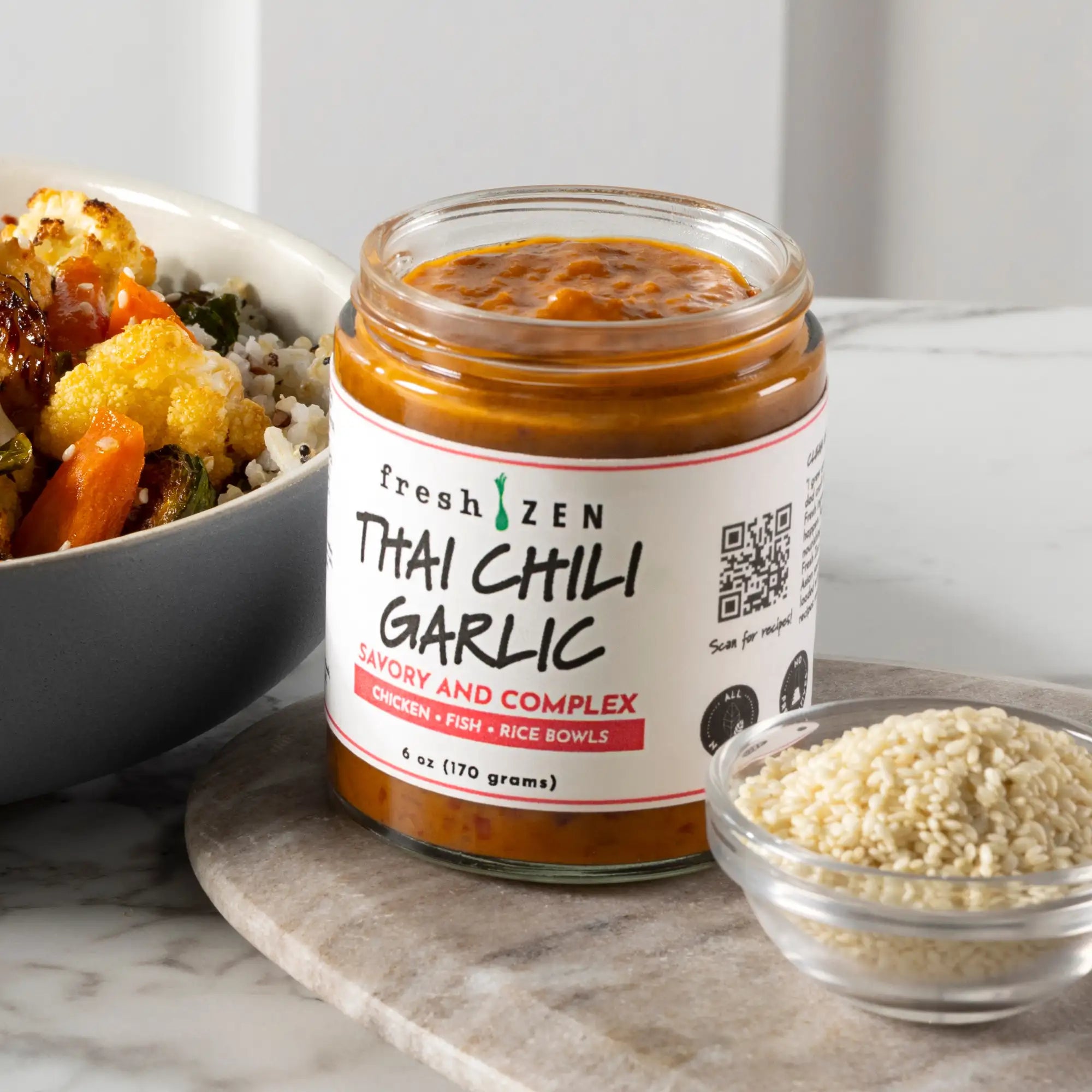 A glass jar of fresh zen thai chili garlic sauce, featuring a white label with black and red text, filled with an orange-red paste.