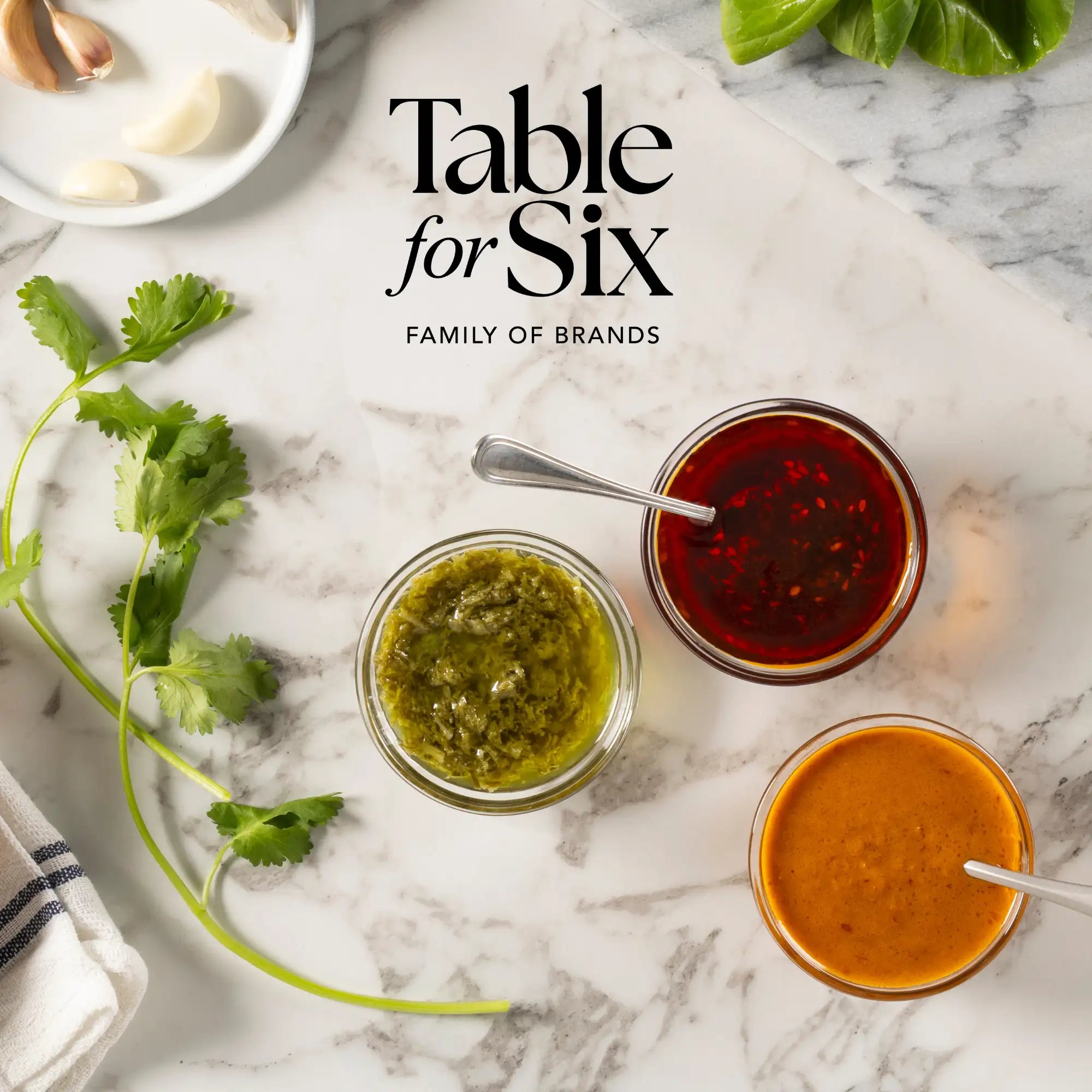 Three glass jars filled with vibrant green, red, and orange sauces sit on a marble surface.