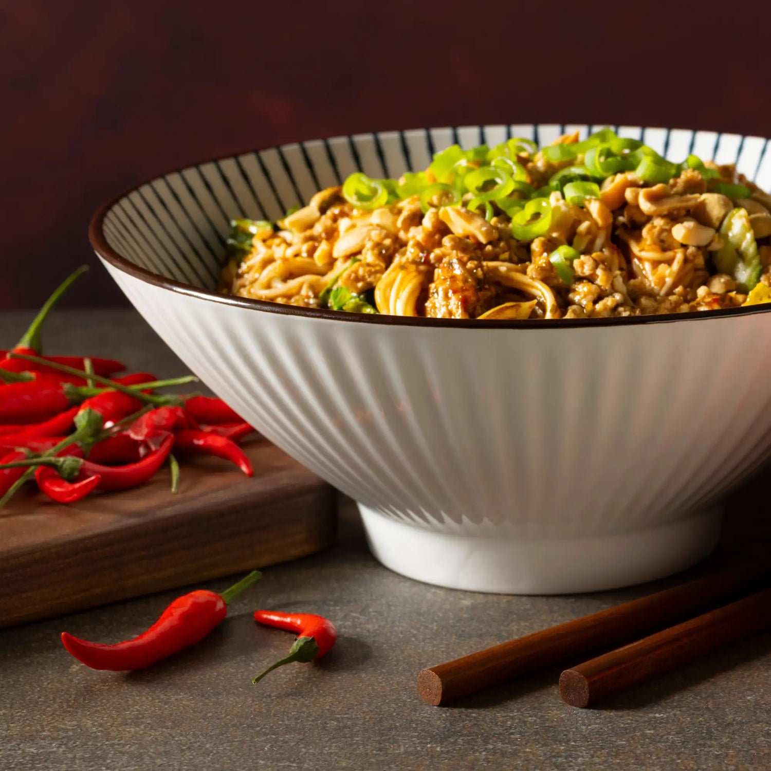 A white ceramic bowl with a ribbed exterior and black-striped rim, filled with stir-fried noodles topped with green onions.