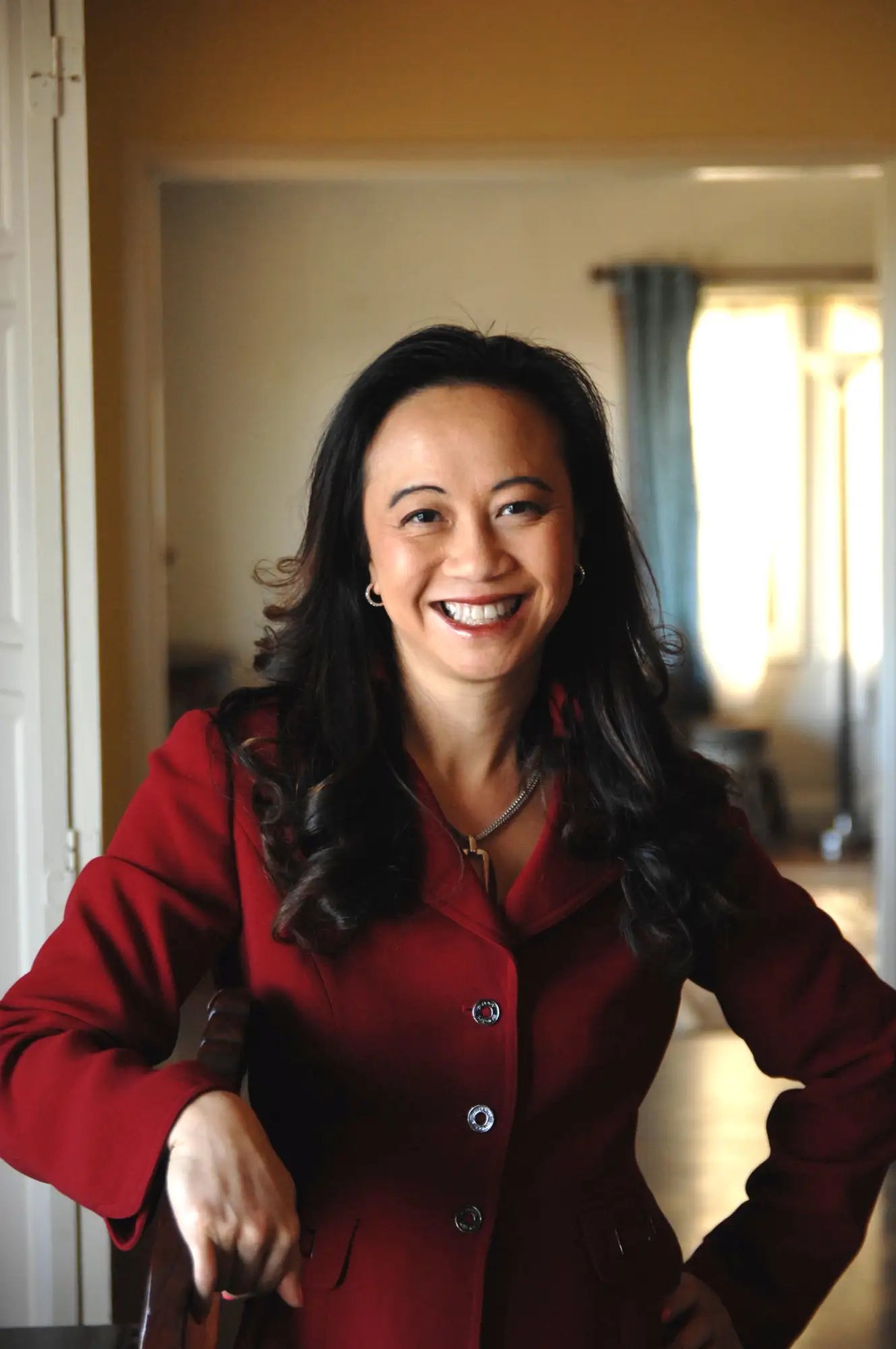 A woman wearing a rich red blazer with silver buttons and a matching necklace.