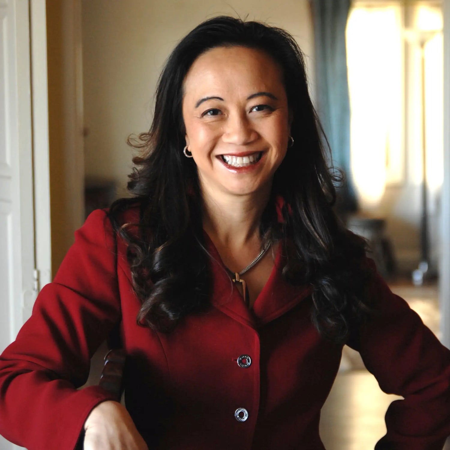 A woman wearing a rich red blazer with silver-toned buttons and a matching necklace.